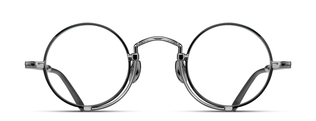 Optical glasses frames are pictured, displaying a frontal view. The glasses feature a round lens shape outlined in black and a M + N engraving along the rim wire. The glasses are stylized with a Pince-nez inspiration.