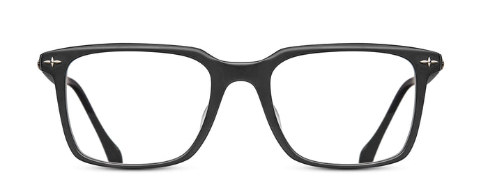 A square-shaped optical glasses frame is pictured. The color of the frame is a matte black and features a silver filigree detailing in each corner of the temple. 