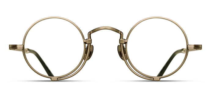 A gold optical glasses frame is pictured. The glasses have a round lens shape and feature an engraving along the rim wire.